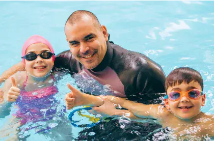 Swim instructor supports two children in the water wearing goggles
